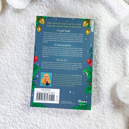 The back cover of the book, styled flat on a white textured fabric background. The cover features a dark teal background decorated with green holly leaves, red berries, gold bells, and white stars, with a small portrait of a woman in a red dress and a barcode at the bottom left.