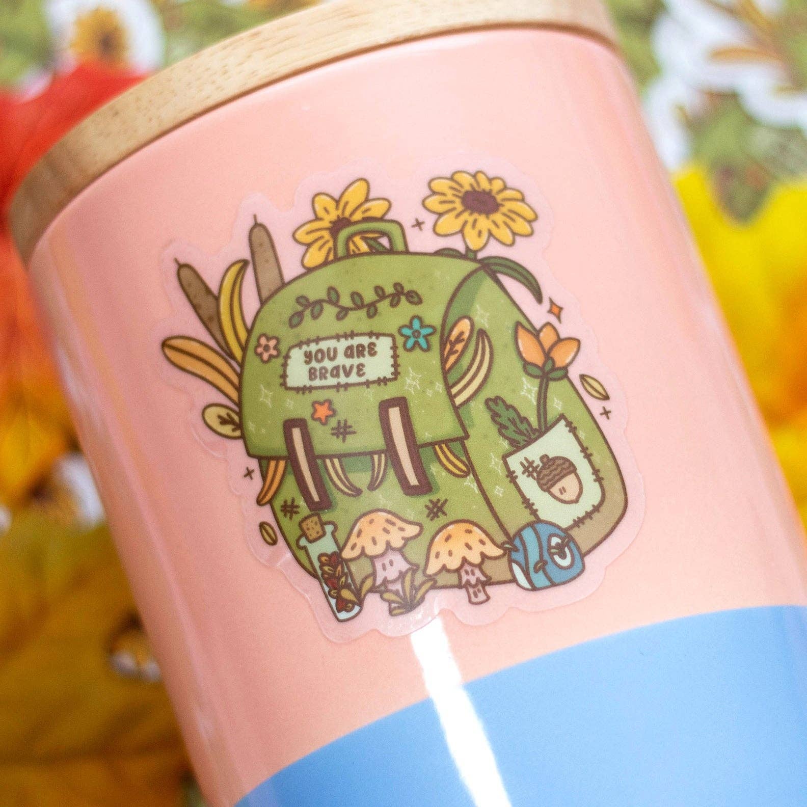 Pink mug with a green illustration of a backpack and flowers on a blurred autumn leaf background