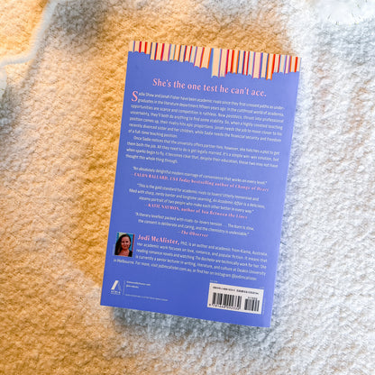 The back cover of the book 'She's the one test he can't ace.' by Jodi McAlister, photographed flat on a textured white and gray blanket.