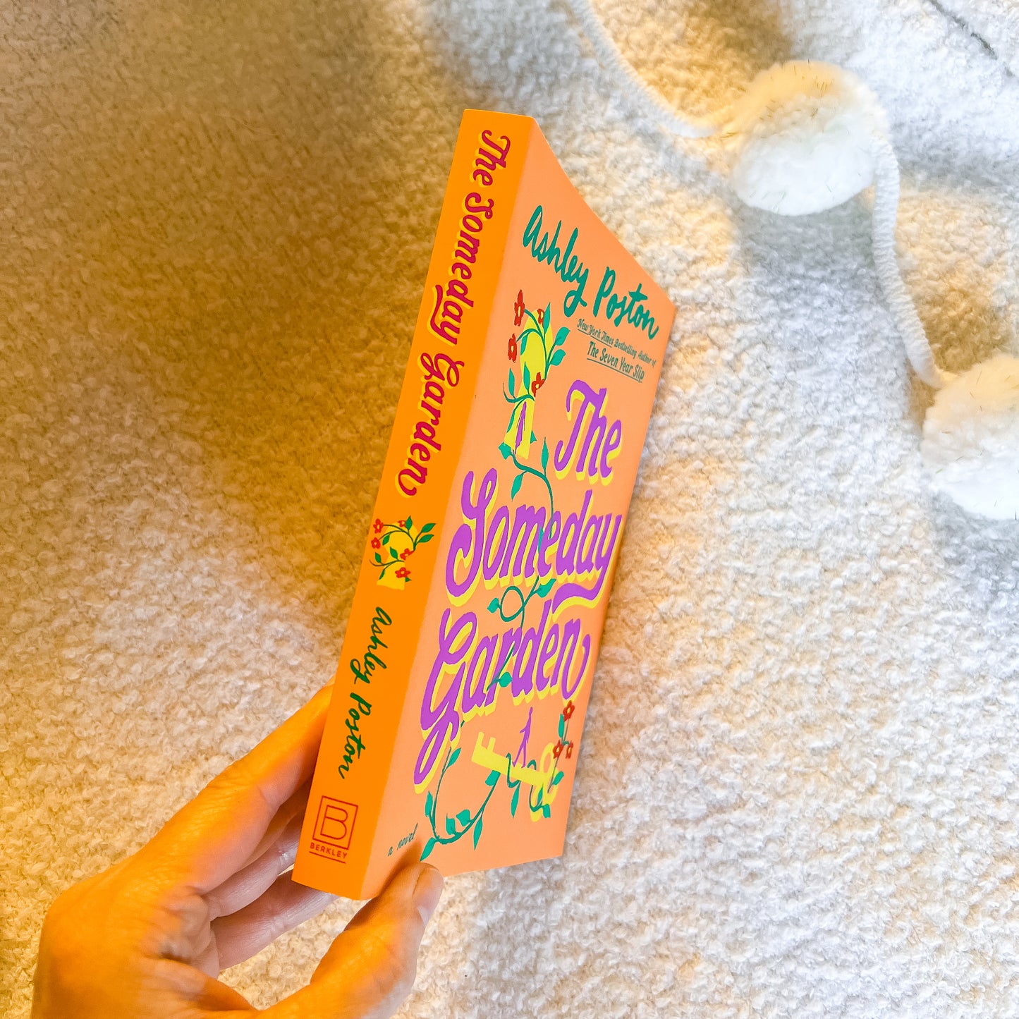 Two books titled 'The Someday Garden' held by a hand on a textured surface.