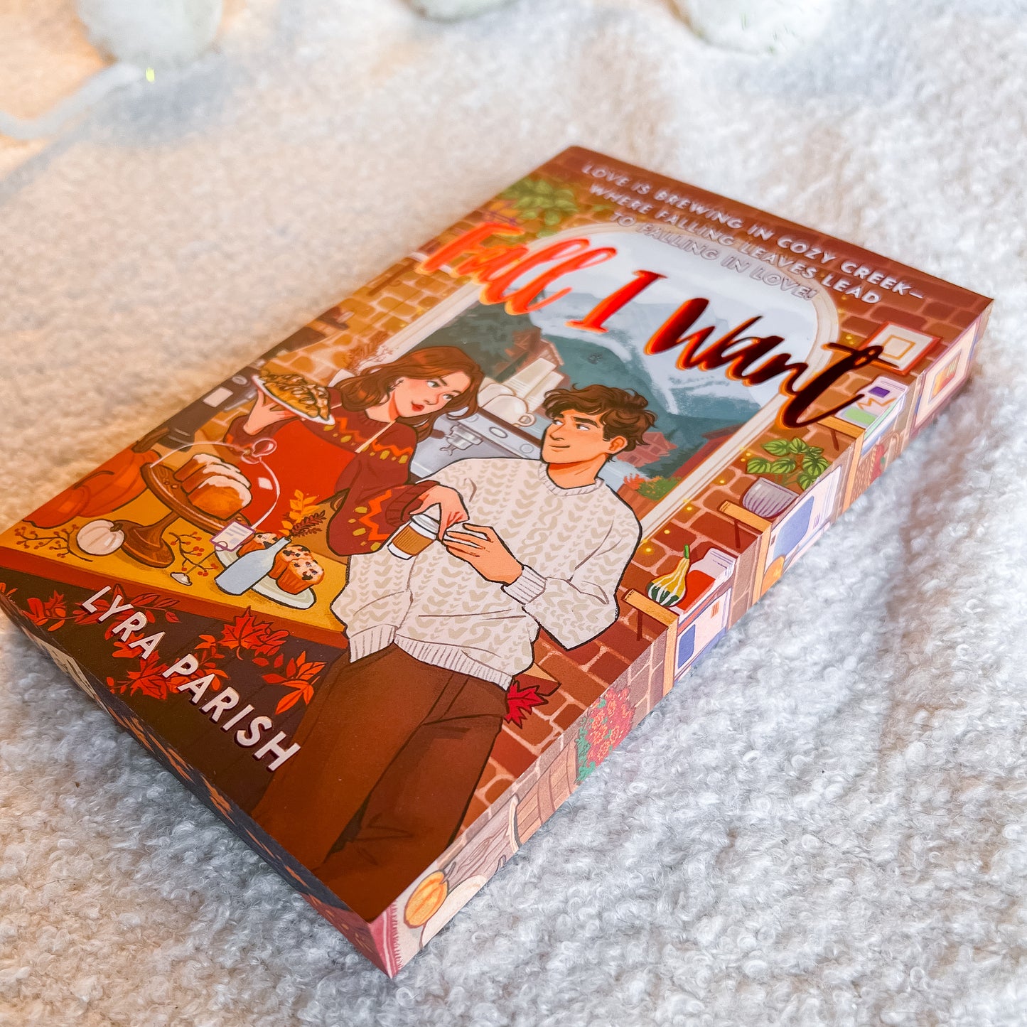 Book box for 'All I Want' by Lyra Parish, featuring an illustrated autumn romance scene, photographed on a soft white textured blanket.
