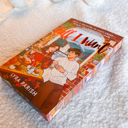 Book box for 'All I Want' by Lyra Parish, featuring an illustrated autumn romance scene, photographed on a soft white textured blanket.