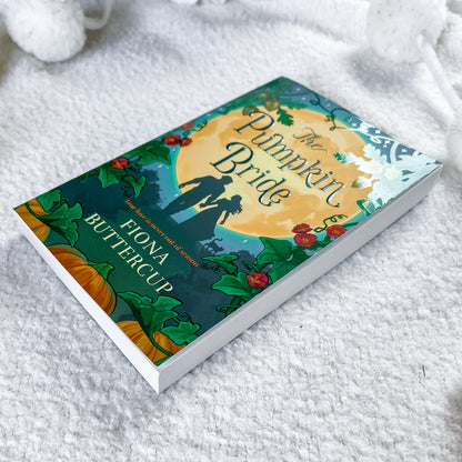 A hardcover book titled "The Pumpkin Bride" by Fiona Buttercup lies on a soft white textured blanket. The cover features a detailed autumn illustration with a large yellow pumpkin, orange pumpkins, green leaves, red berries, and a silhouette of a bride and groom.