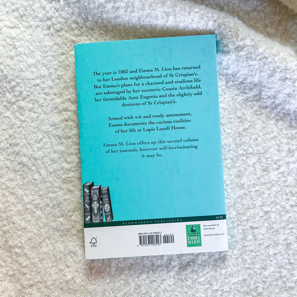 The back cover of a book titled 'Emma M. Lion' lies flat on a textured white fabric surface.