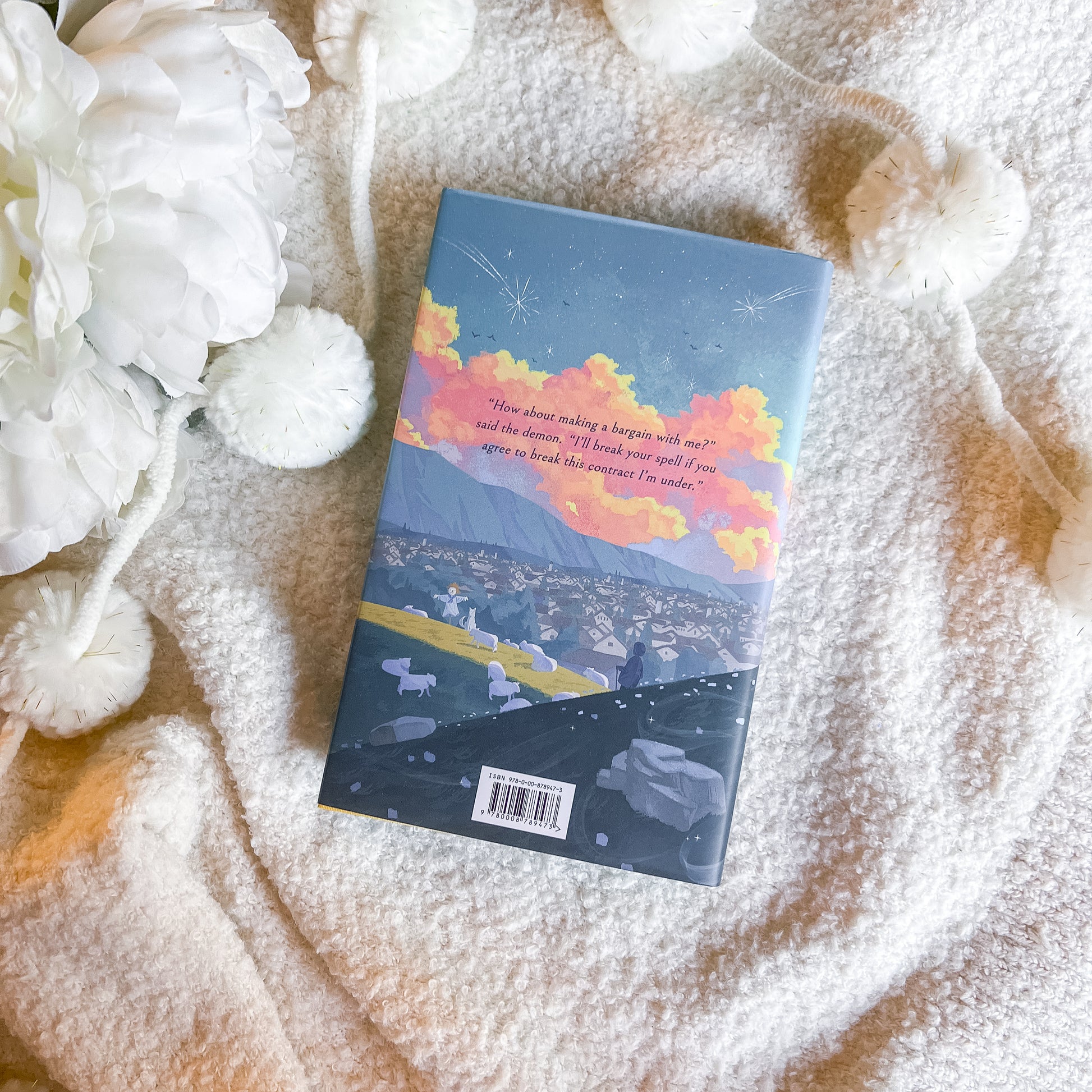Book with a colorful cover featuring a landscape and text, placed on a textured surface with white flowers.