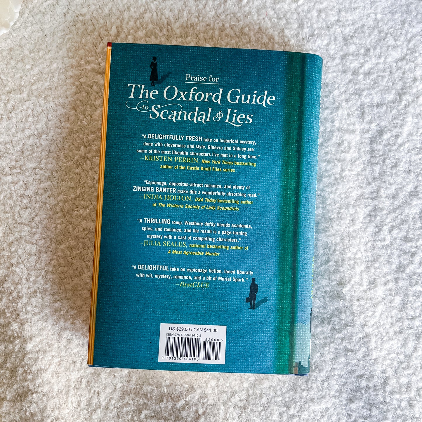 The back cover of a book titled 'Praise for The Oxford Guide to Scandal & Lies' is shown flat on a textured white fabric background. The cover features a teal-to-dark-teal gradient with white text and small black silhouettes.