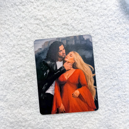 A rectangular art print or card featuring a painted couple embracing, placed on a textured white fabric background.