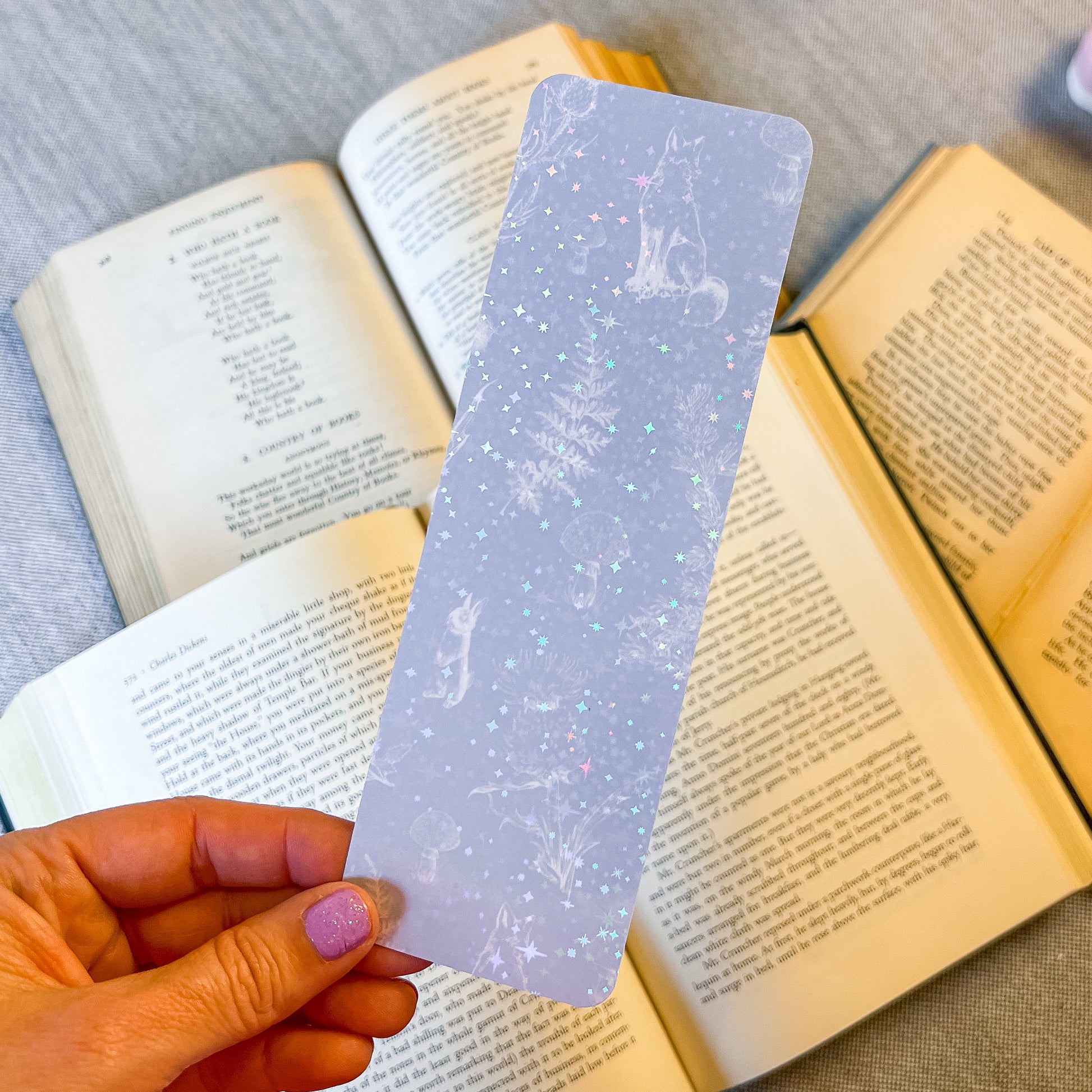 Hand holding a decorative bookmark over open books on a textured surface