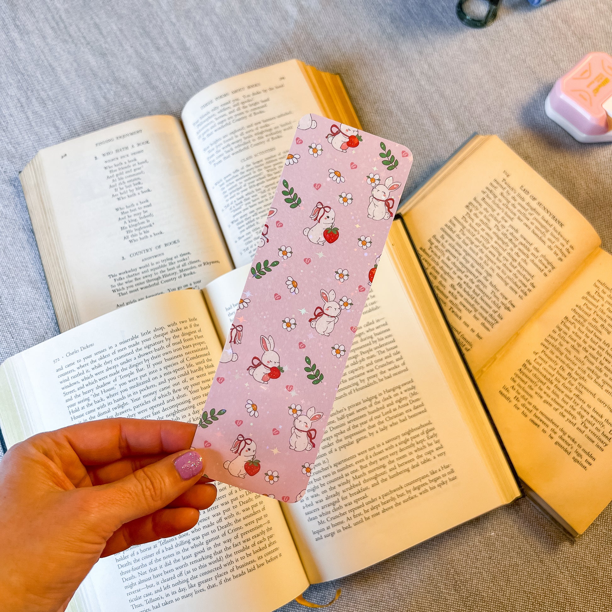 Hand holding a pink bookmark with cartoon designs over open books.