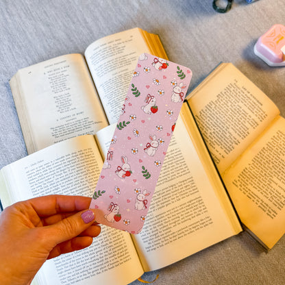 Hand holding a pink bookmark with cartoon designs over open books.