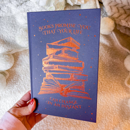 Book with a stack of books illustration and text on a blue background, held against a textured fabric background.