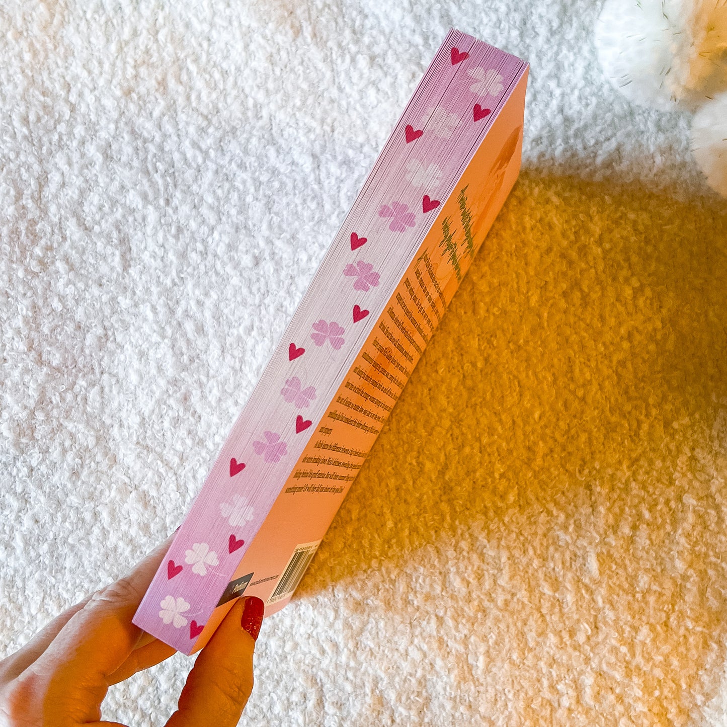 Book with pink and white design held by a hand on a textured surface