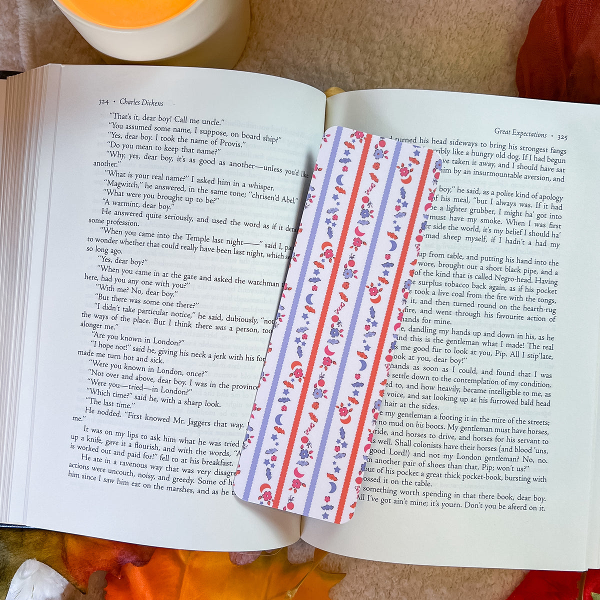 An open book spread showing printed pages with a decorative orange and purple floral bookmark or ribbon attached on the right page, photographed from above on a neutral surface.