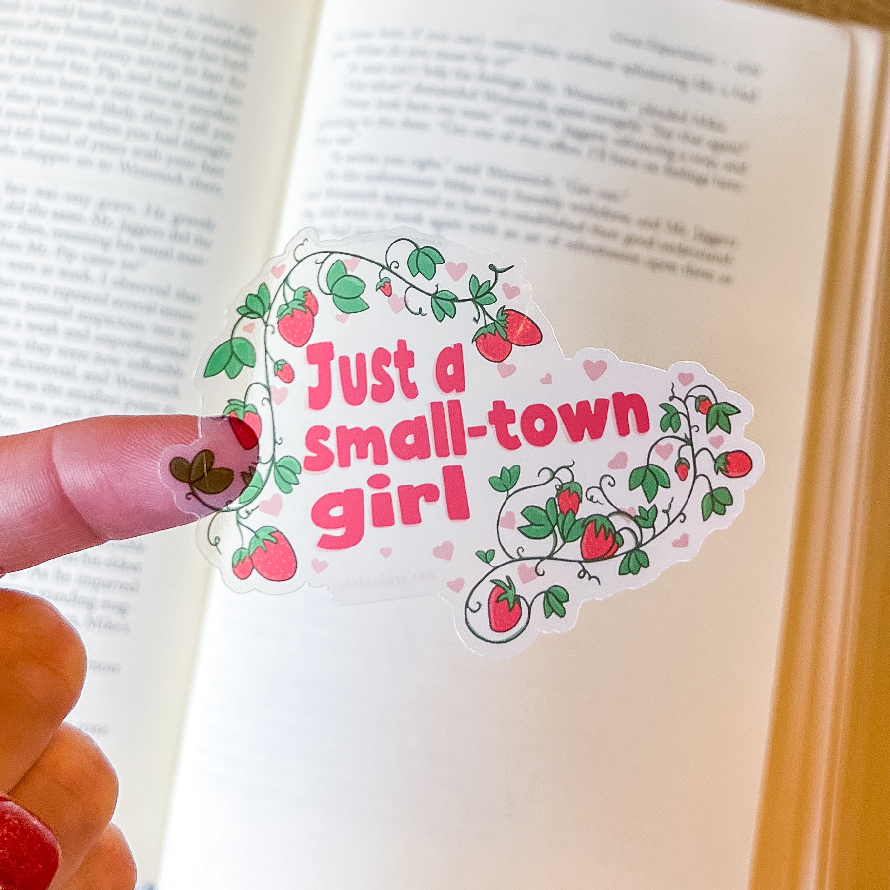 Sticker with 'Just a small-town girl' text held over an open book