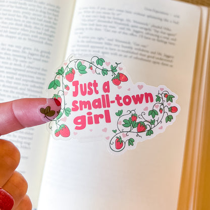 Sticker with 'Just a small-town girl' text held over an open book