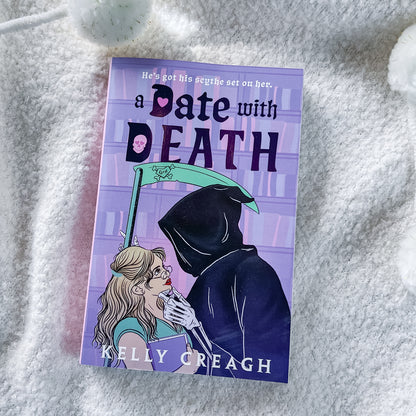 A book titled 'a Date with DEATH' by Kelly Creagh, featuring a purple cover with an illustration of a woman and a grim reaper, photographed on a soft white textured blanket.