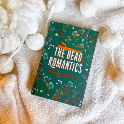 Book titled 'The Dead Romantics' by Ashley Poston on a soft fabric background with flowers.