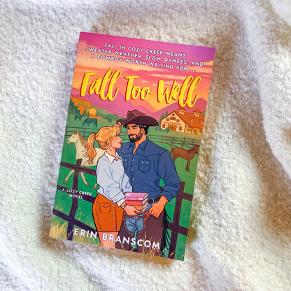 A book titled "Fall Too Well" by Erin Branscom, featuring a colorful illustrated cover with a cowboy and cowgirl in a farm setting, placed on a white textured blanket.