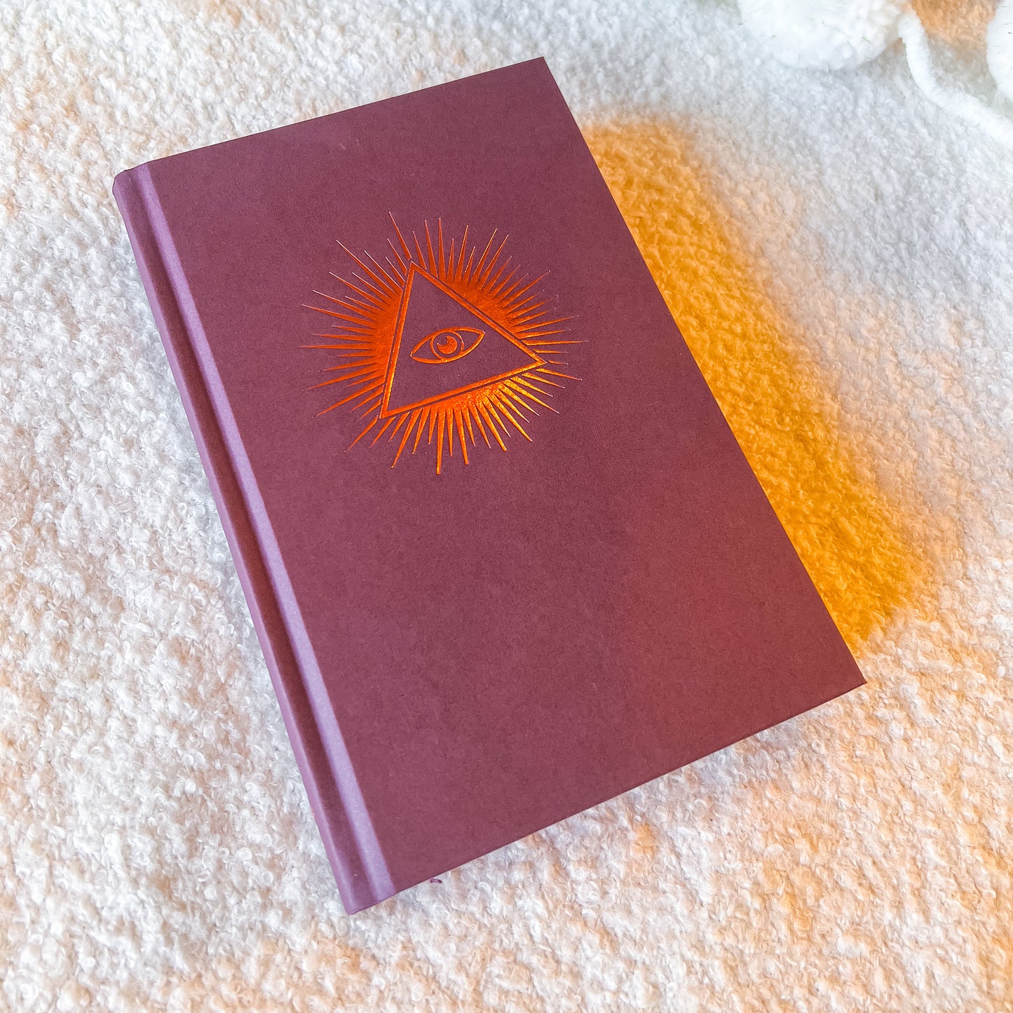 Maroon notebook with orange eye design on a textured surface