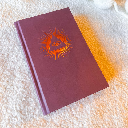 Maroon notebook with orange eye design on a textured surface