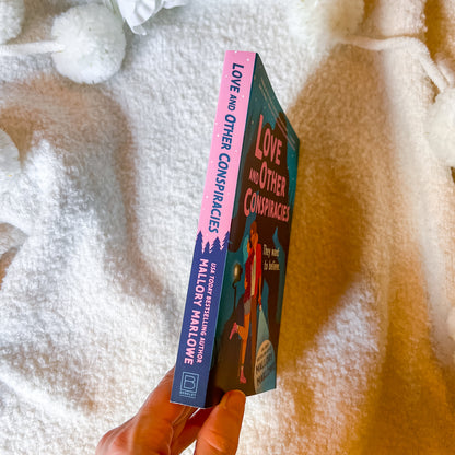 Book titled 'Love and Other Conspiracies' held against a textured white and brown background