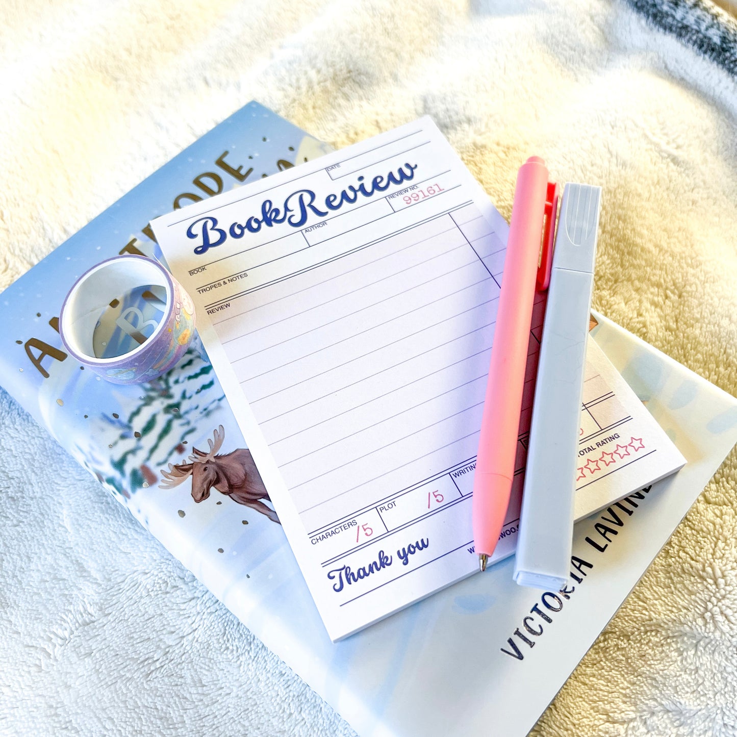 Notebook with 'Book Review' template on a magazine with a pink pen and white highlighter.