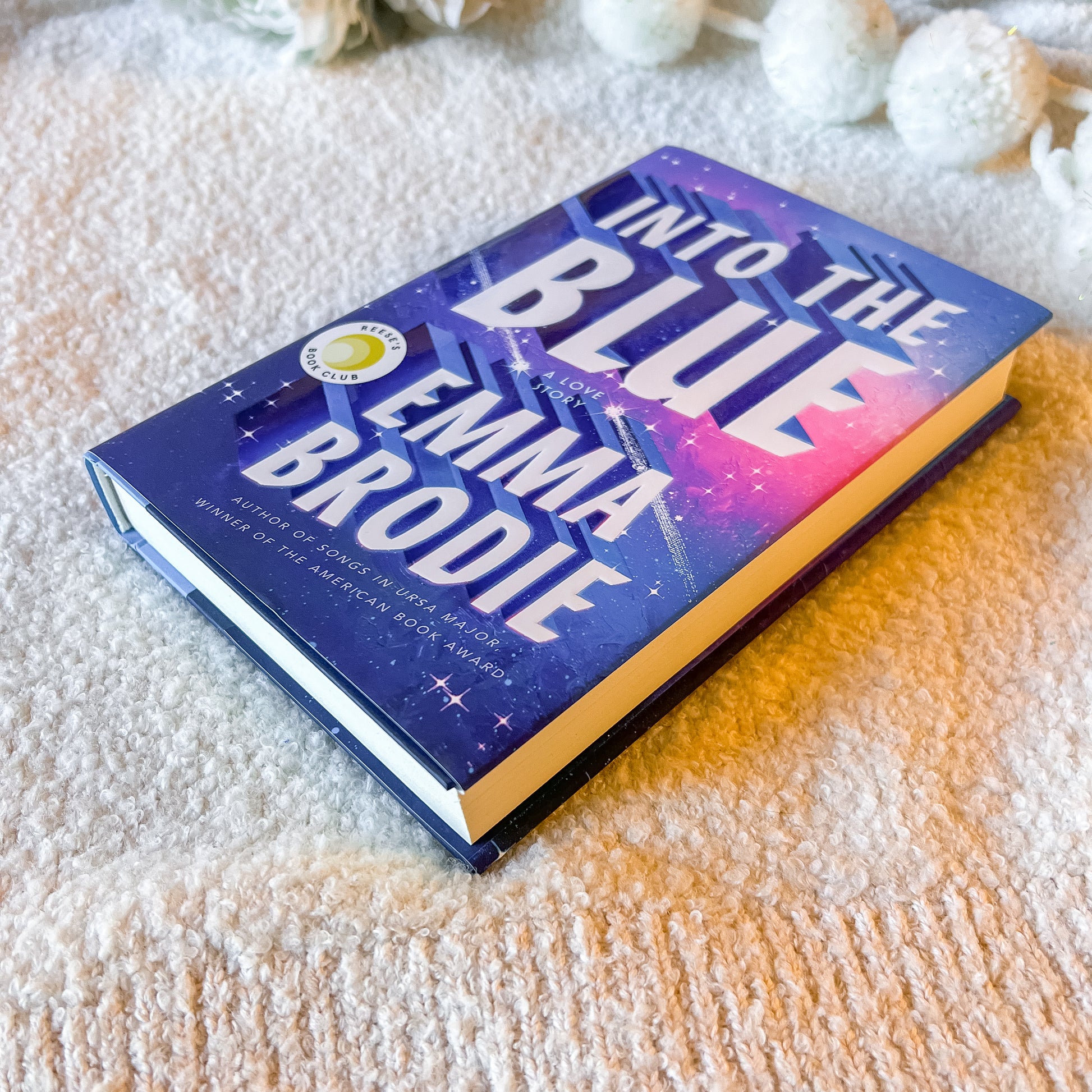 Book titled 'Into the Blue' by Emma Brodie on a textured surface with decorative elements.