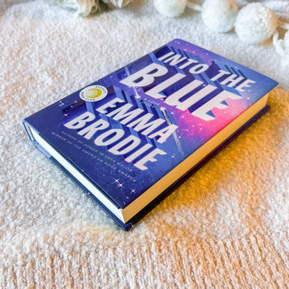 Book titled 'Into the Blue' by Emma Brodie on a textured surface with decorative elements.