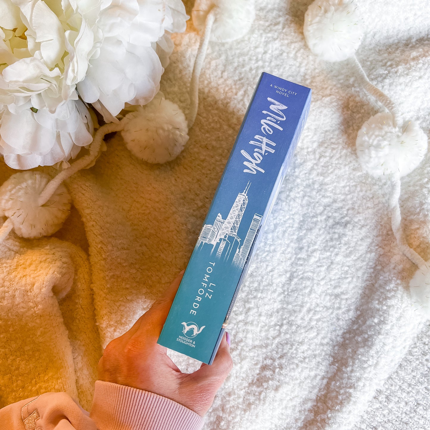 Hand holding a book spine with a white flower arrangement in the background