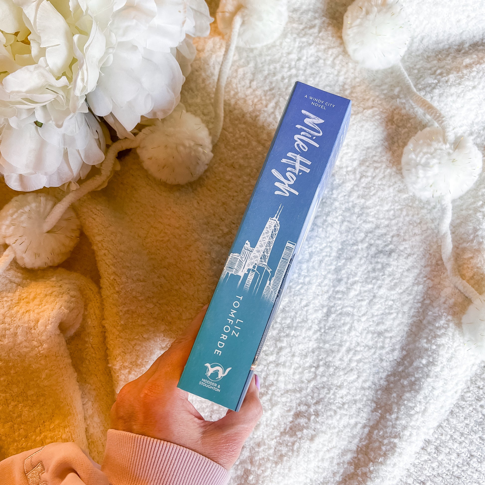Hand holding a book spine with a white flower arrangement in the background