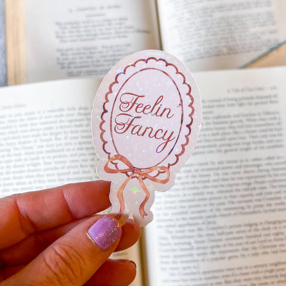 Sticker with 'Feelin' Fancy' text held over an open book