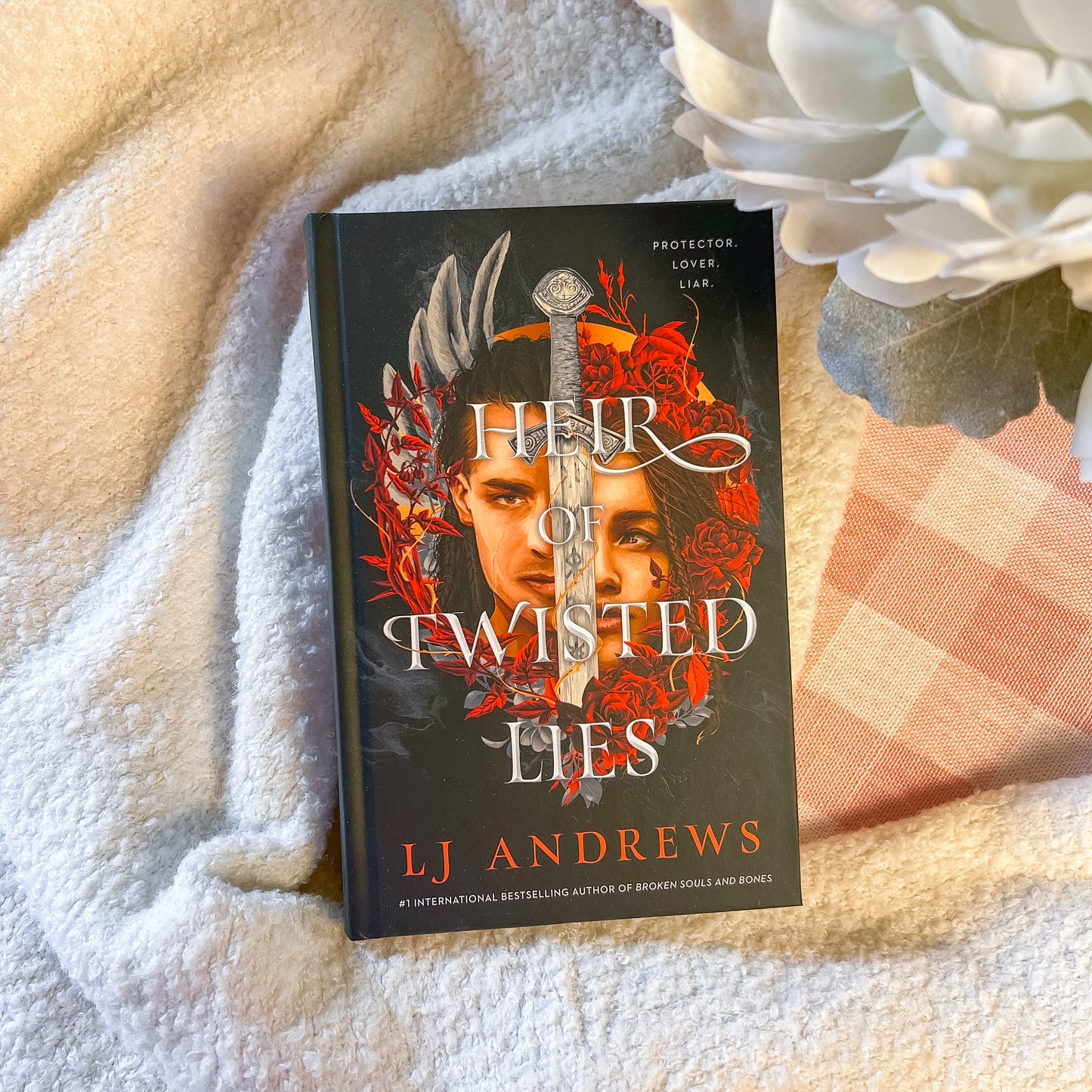 Book titled 'Heir of Twisted Lies' by L.J. Andrews on a textured surface with flowers.
