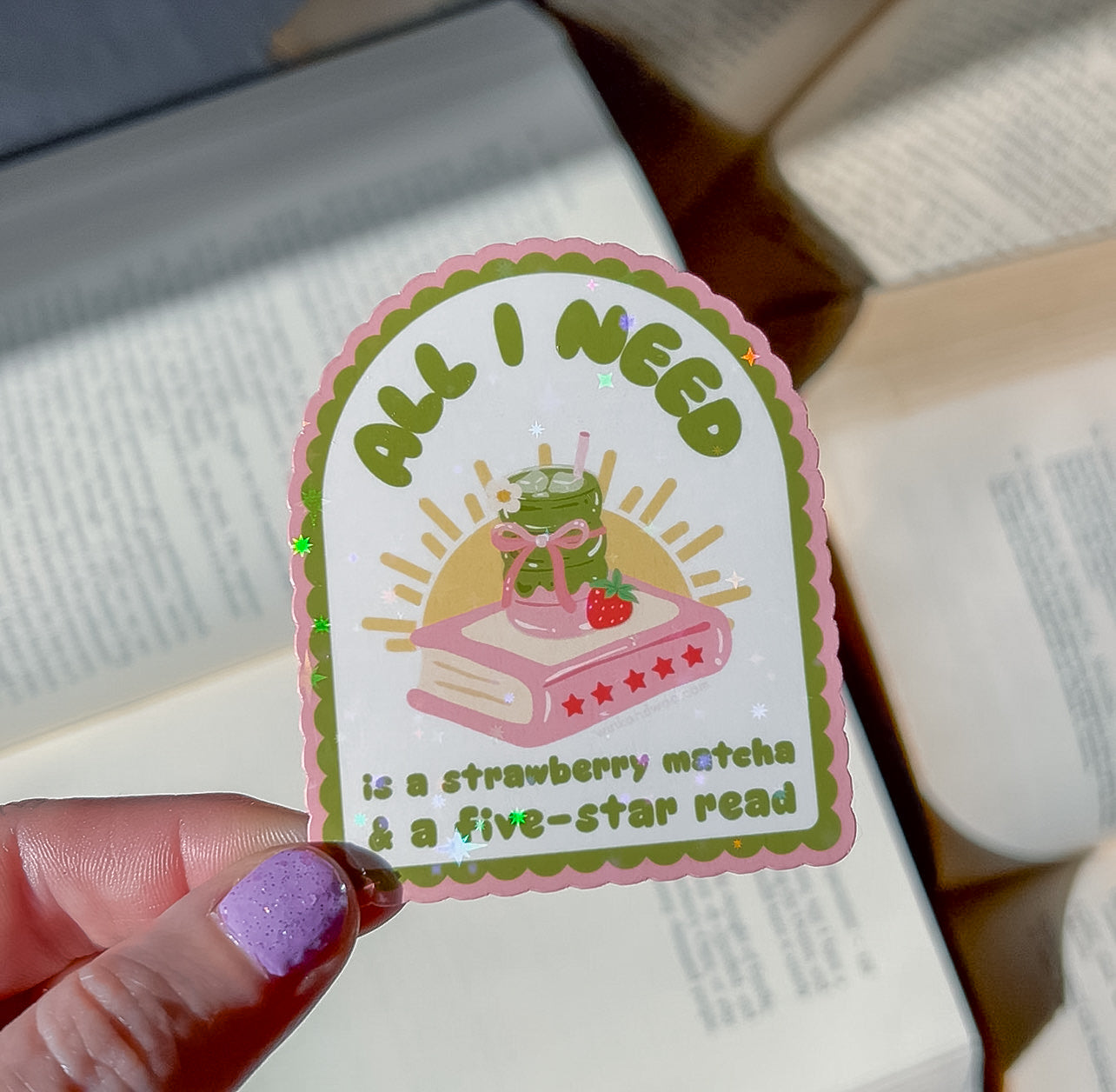 Sticker with text 'All I Need is a Strawberry Matcha & a Five-Star Read' held by a hand.