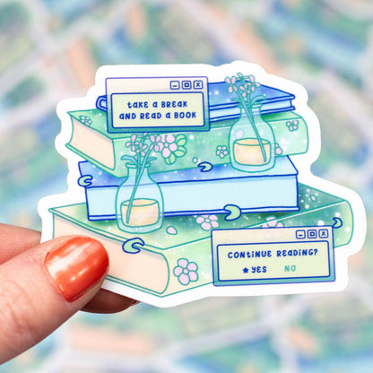 Sticker with book-themed design held by a hand against a blurred background