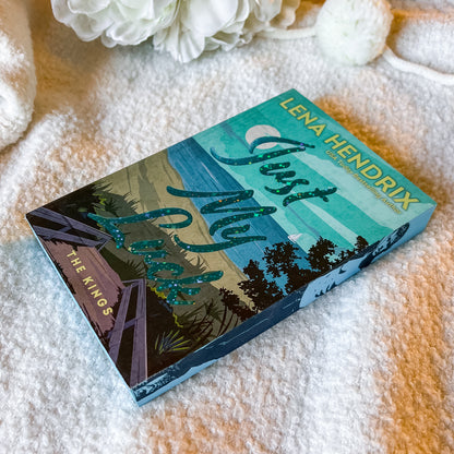 Book titled 'Just My Luck' by Lena Hendrix on a textured surface with white flowers.