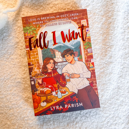 A paperback book titled 'Fall I Want' by Lyra Parish, featuring a colorful autumn-themed illustration of a couple on the cover, placed on a soft white textured blanket.