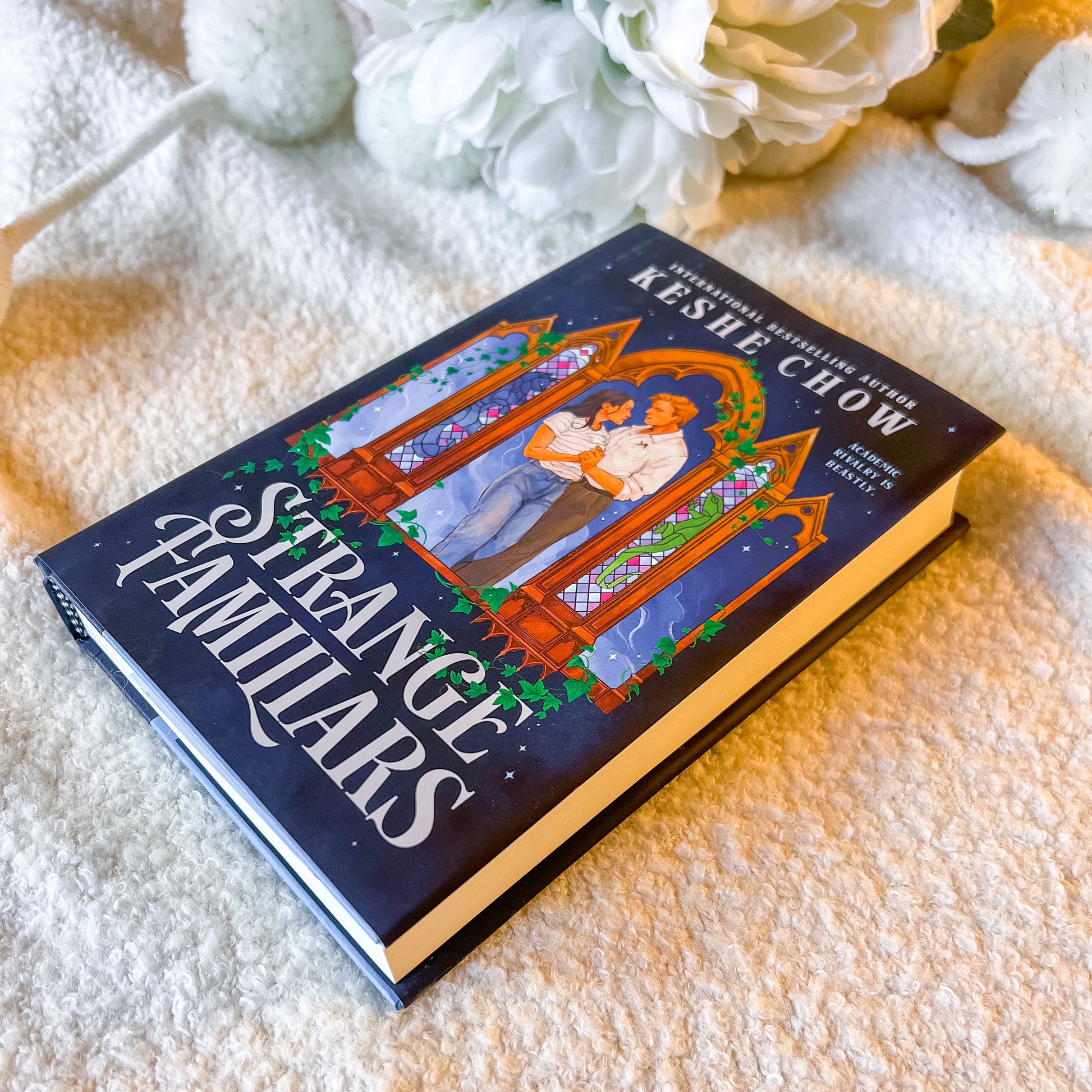 Book titled 'Strange Familiars' by Keslie Chow on a textured surface with flowers in the background