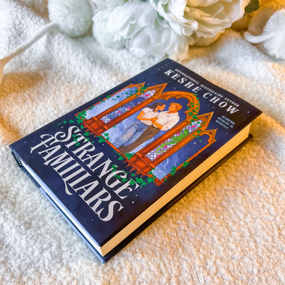 Book titled 'Strange Familiars' by Keslie Chow on a textured surface with flowers in the background