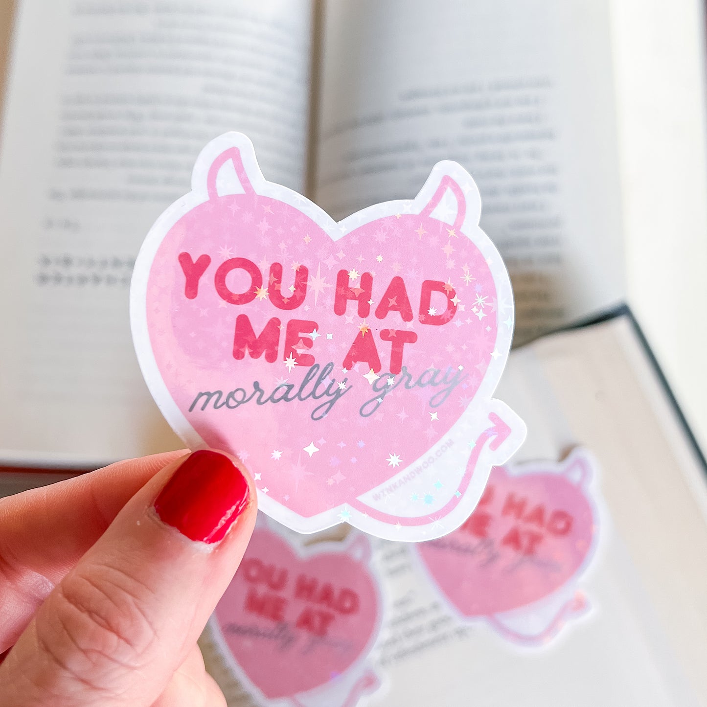 Pink heart-shaped sticker with text held by a hand over an open book