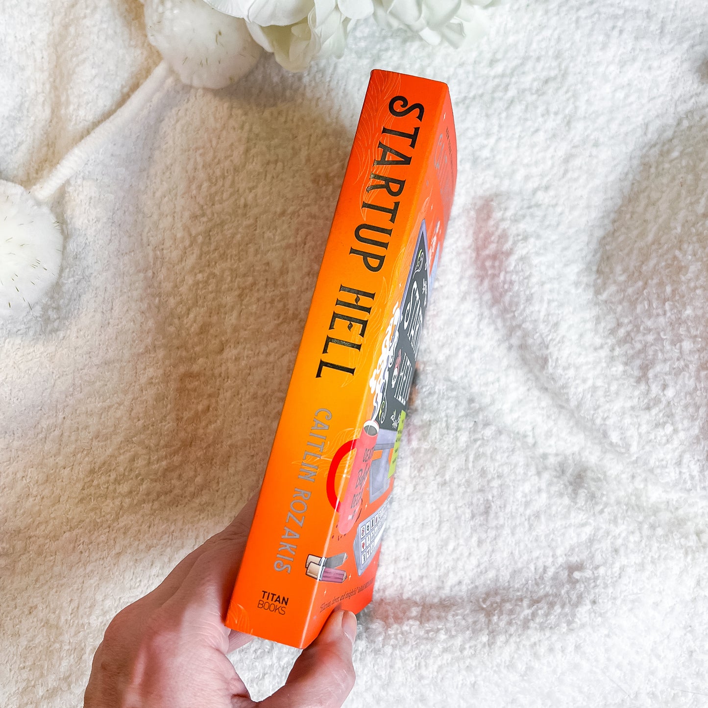 Book titled 'Startup Hell' held by a hand on a textured surface