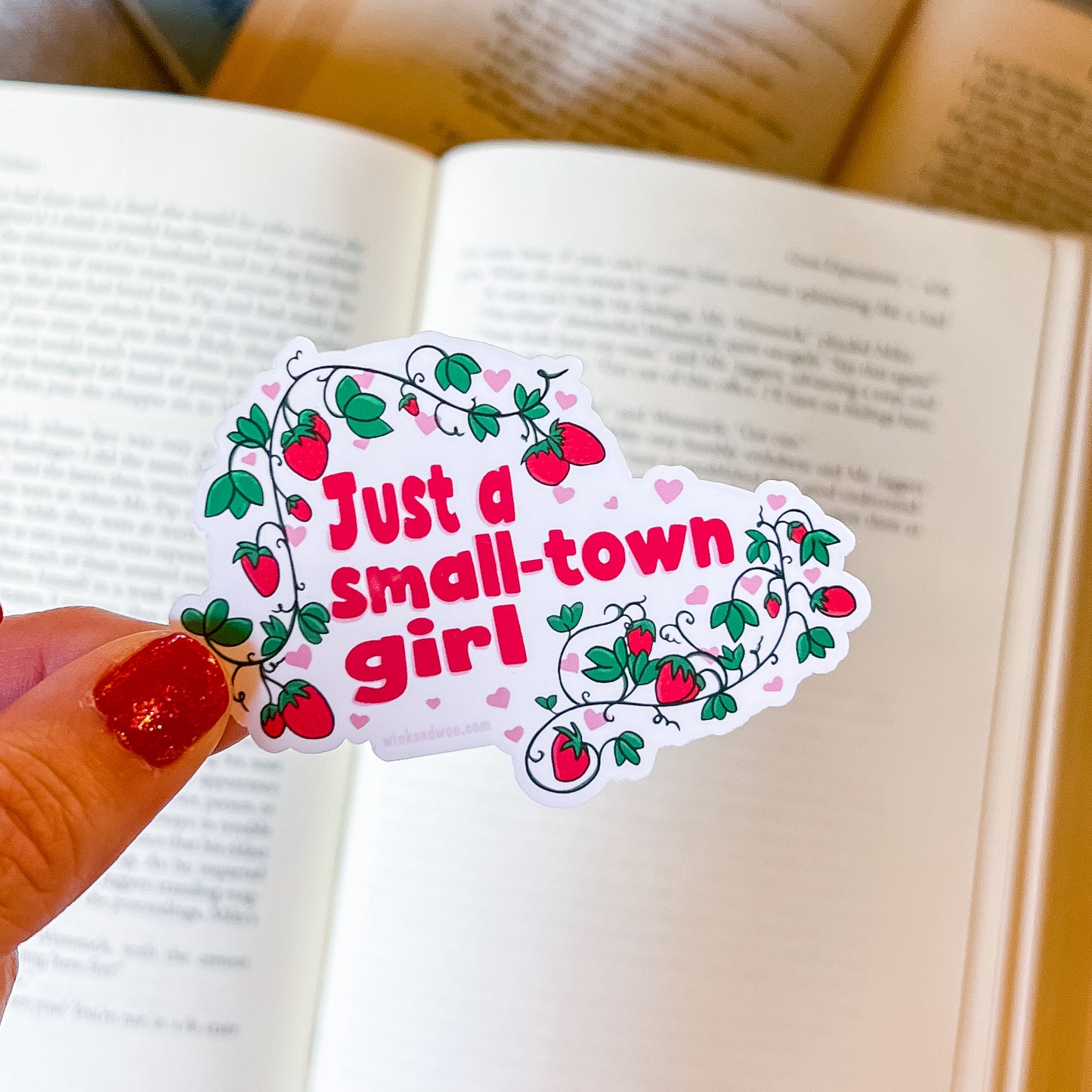 Sticker with 'Just a small-town girl' text held over an open book