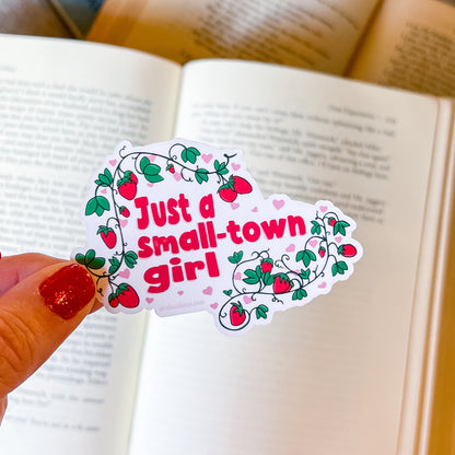 Sticker with 'Just a small-town girl' text held over an open book