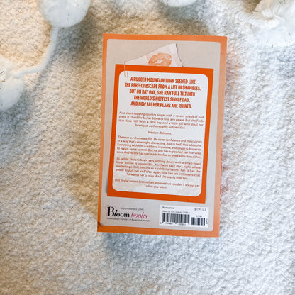 The back cover of a book by Bloom Books, featuring an orange border and white background with black text, photographed flat on a white textured blanket.