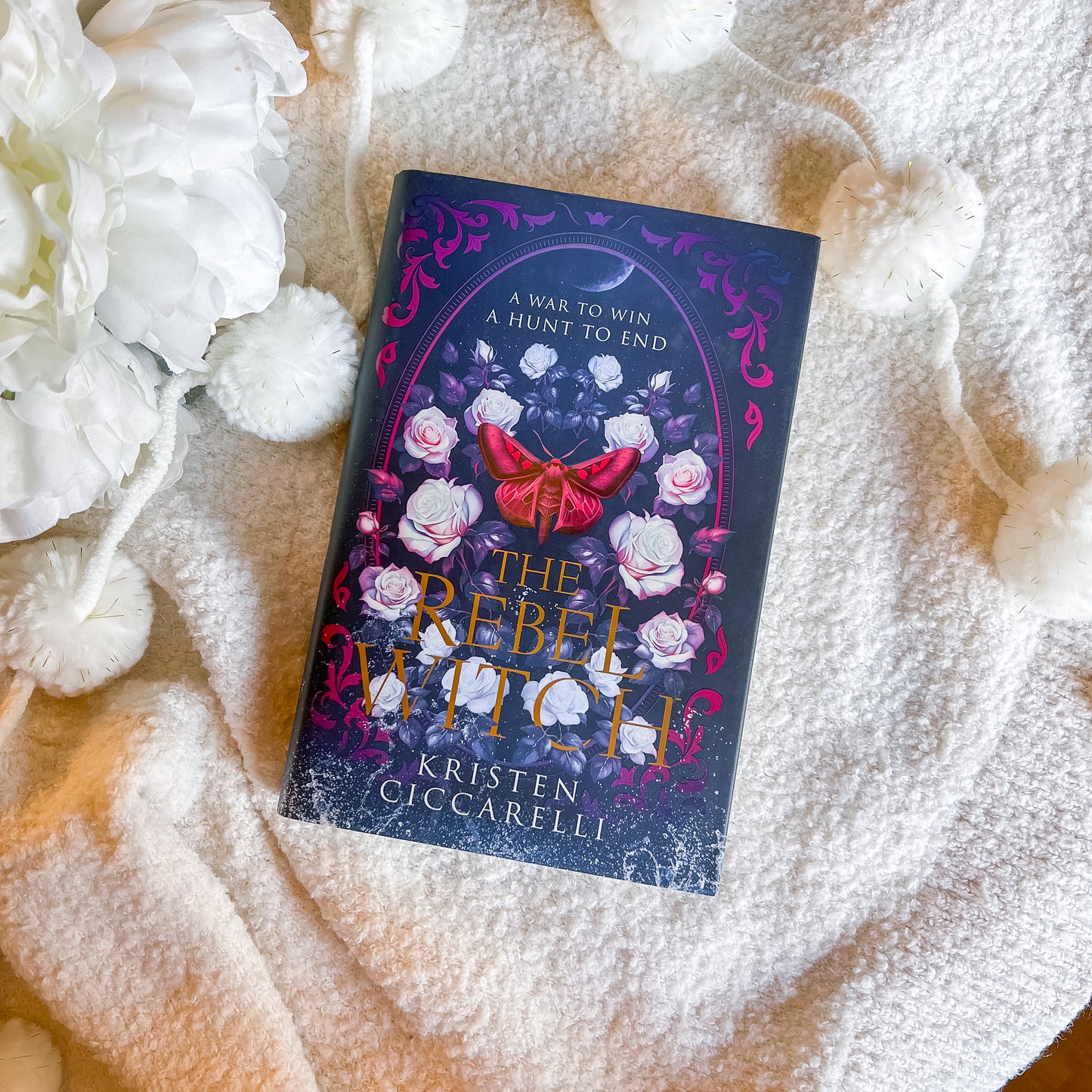Book titled 'The Rebel Witch' by Kristen Ciccarelli on a textured surface with flowers.