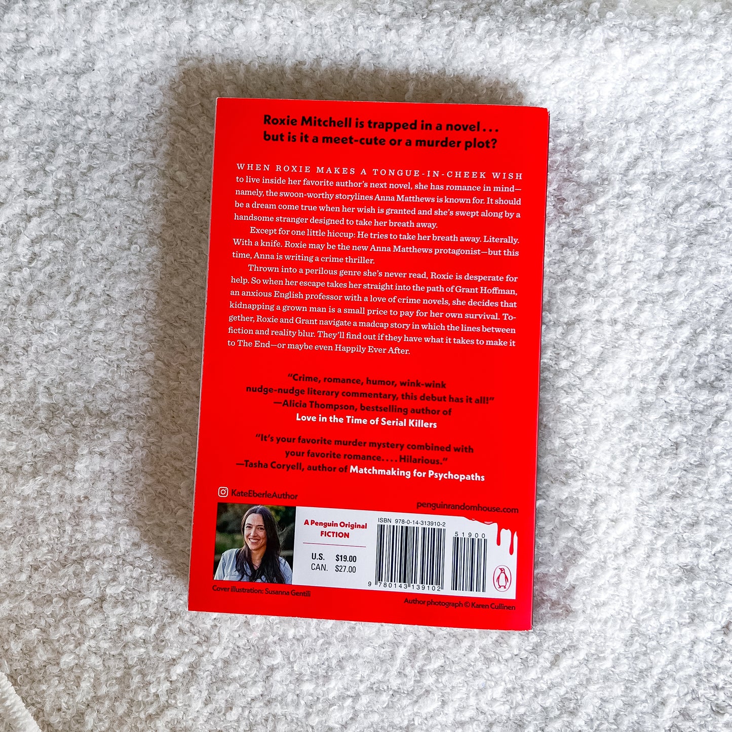 The back cover of the book 'The End or the End Again' by Katie Cahill, featuring a bright red background with black text, a barcode, and a small author photo, photographed flat on a textured gray fabric background.