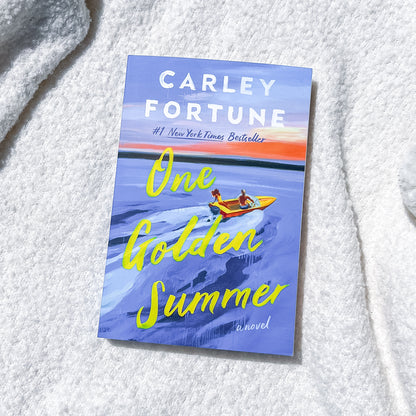Book cover of 'One Golden Summer' by Carley Fortune on a textured white surface