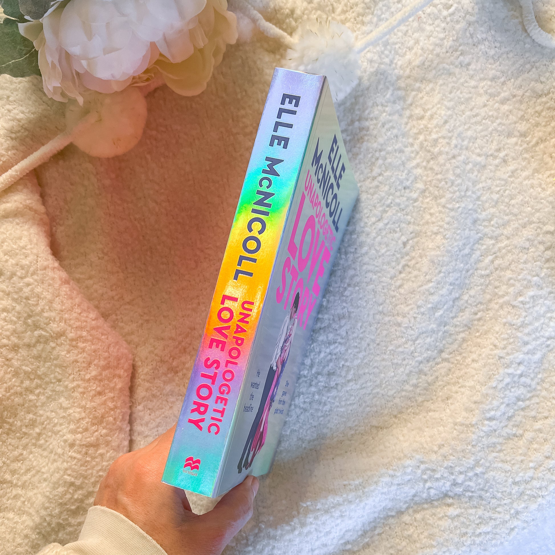 Book titled 'Unapologetic Love Story' by Elle McNicoll held against a soft, light background.