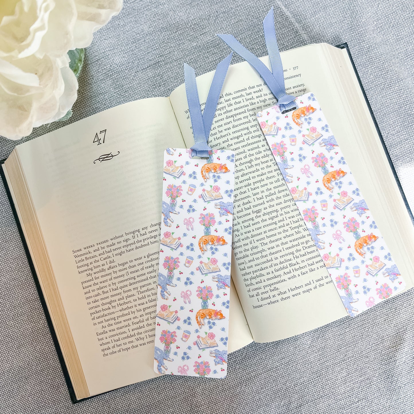 Floral and cat patterned bookmark with a blue ribbon lying on top of a book.