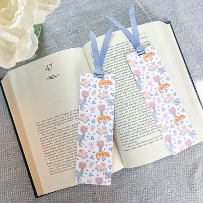 Floral and cat patterned bookmark with a blue ribbon lying on top of a book.