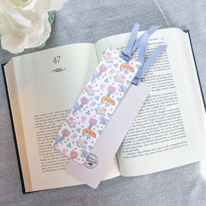 Floral and cat patterned bookmark with a blue ribbon lying on top of a book.